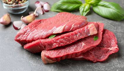 Cut fresh beef meat with basil leaves on grey table, closeup