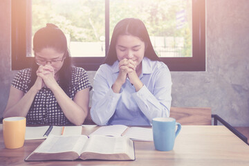A adult Christian  woman  praying with her your woman friend with the open bible and acup of coffee on wooden table at church prayer room ,Christian fellowship, disciple concept