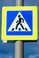 Close-up pedestrian crossing sign with bright yellow frame on cloudy dark blue sky background.