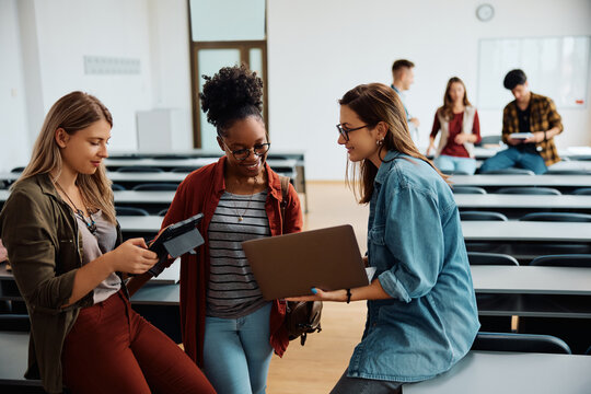 Happy female students using wireless technology in lecture hall.