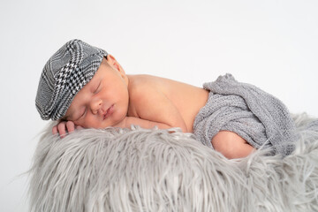 Baby Junge Newborn mit Mütze liegend auf grauem Fell in einem Eimer, weißer Hintergrund isoliert...