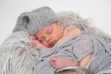 Baby Junge Neugeborenes mit Mütze liegend auf grauem Fell in einem Eimer, weißer Hintergrund...
