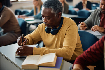 Senior black man writes notes while learning during adult education training class in classroom.