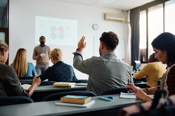 Fotobehang Back view of older student raising his hand to answer teacher's question during education training class. © Drazen