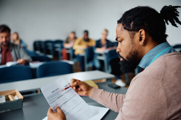Black teacher examining assignments of adult students during class in lecture hall.
