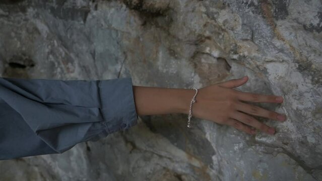 Closeup hand of young girl gently touches rock wall in the cave and moving forward. Female palm sliding hand against rough surface of old ancient stone in slow motion. 