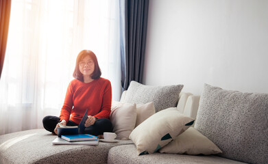  An Asian elderly woman is sitting on the sofa and reading a book.