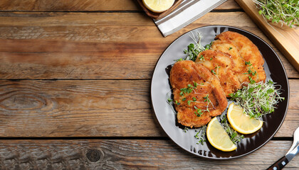 Tasty schnitzels served with lemon and microgreens on wooden table, flat lay. Space for text