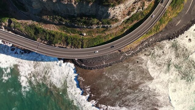 Drone aerial view of Coastline highway with traffic driving car on the road and mountain cliff coastal beach at NSW, Australia. Landmark famous place, beauty nature and land transportation concept.