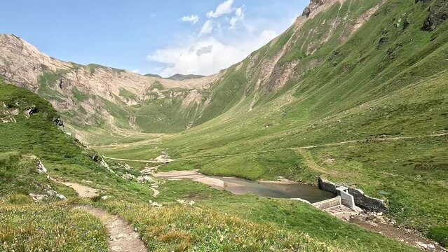 Lush green mountain valley with a small river and a dam. Summer day in the alps of Italy  in fornt of Grieshorn pass
