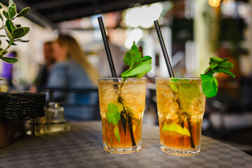 Alcohol drink. On Table cafe outdoors. glasses with alcohol drink and half lime,mint leaves. cocktail mojito with slice lime and mint leaf.City life.Blurred cafe background.Summer evening.