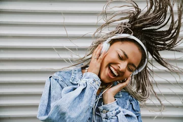 Gordijnen Cheerful woman dancing while listening music with headphones outdoors near gray wall © Drobot Dean
