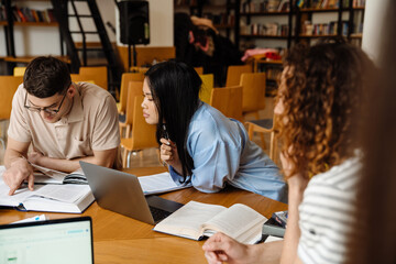 Group of multiethnic students preparing for exams together while sitting in library