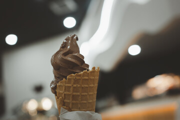 Hand holding chocolate ice cream in waffle cone. Close up