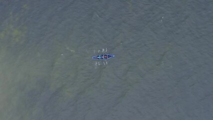 Drone rotates above and follows currach boat rowers in open ocean water splashing