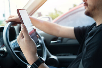 Young man reading messages holding a cell phone while driving. Dangerous behavior, accident risk. - obrazy, fototapety, plakaty