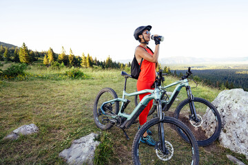 Fototapeta premium Cyclist woman standing with bike and drinking water