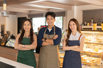 Asian barista male and female colleagues standing with arm crossed and looking at camera and smiling at cafe shop. Happy working a small business together