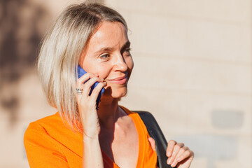 Happy middle aged woman outside in city with mobile phone