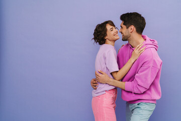 Cheerful man and woman hugging while standing isolated over purple background