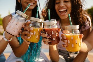 Group of women clinking juice glasses while spending time together in park