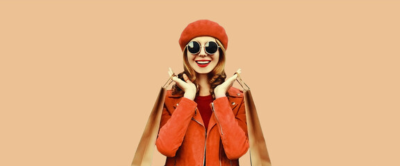 Autumn portrait of beautiful happy smiling young woman with shopping bags wearing red jacket, beret on brown background