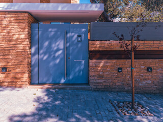 A contemporary house entrance with a gray painted iron door between light brown fence walls. Travel to Athens, Greece.