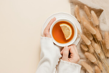 Woman hold cup of tea with lemon, lagurus grass decoration with linen cloth on beige background,...