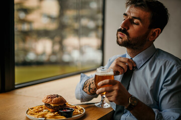 Tired businessman relaxing with a beer and burger after work.