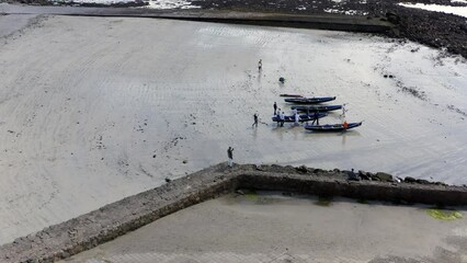 Drone profile view of people carrying currach boats towards waters edge