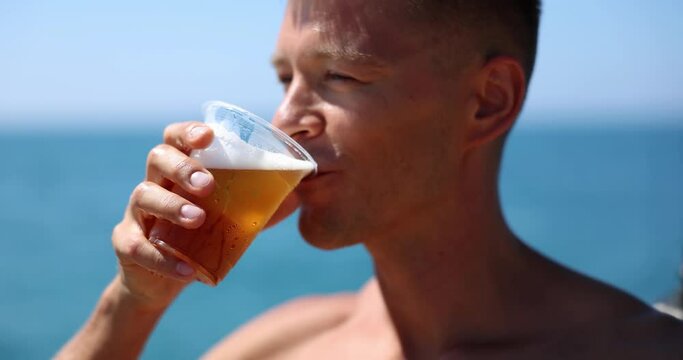 Man drinks beer on beach from plastic cup. Beach party and cold beer for tourists