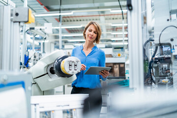 Businesswoman with tablet at assembly robot in a factory