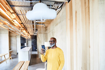 Mature businessman holding cell phone attached to cloud balloon