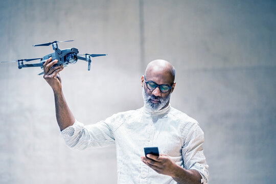 Portrait of bald mature man holding quadcopter while looking at cell phone