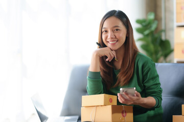Beautiful Asian online business owner is using mobile phone checking with customer to check...