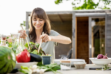 Smiling woman preparing a salad on garden table