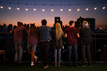 Friends standing under string lights on rooftop