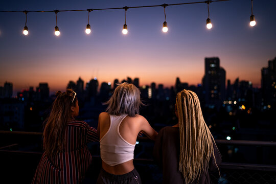 Friends standing under string lights on rooftop at dusk