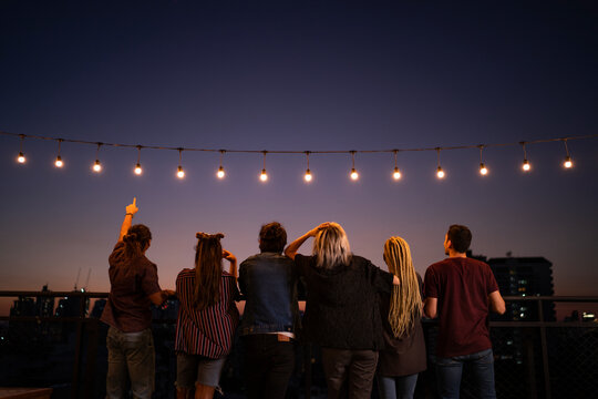 Friends spending leisure time under string lights on rooftop at dusk