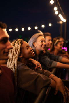 Happy friends having social gathering under string lights on rooftop