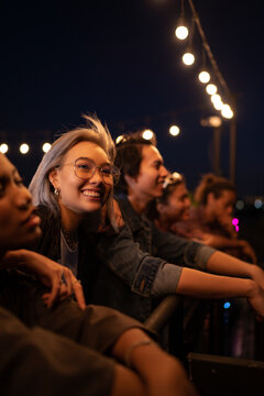 Cheerful friends having social gathering under string lights on rooftop