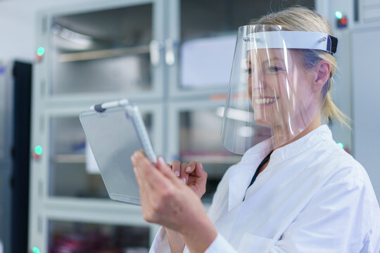 Smiling mature female scientist wearing protective face shield while using digital tablet at laboratory