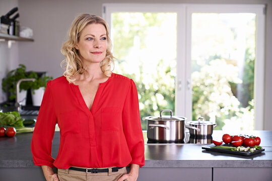 Confident woman wearing red blouse standing in kitchen