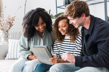 Surprised parents sitting on sofa with daughter holding ring file with school report