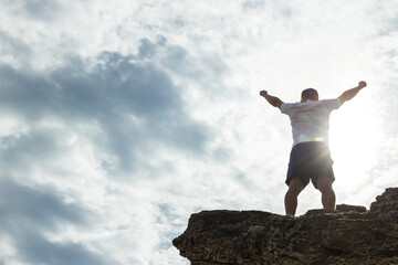 A man on a rock is engaged in energy practices, hands up