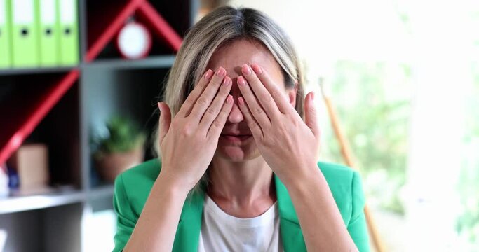 Portrait of young beautiful woman closing eyes with hands standing in office. Embarrassed girl covers eyes with palms ignoring news