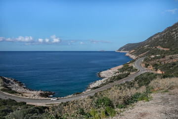 Fototapeta premium Long curved asphalt road running along the rocky shore of the Mediterranean Sea in a Turkish resort. The hilly coast is covered with forest, white stones. Endless deep blue sea on the horizon.