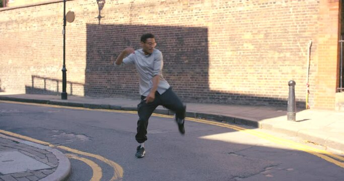 Young man, dancing and happy in street, city and outdoor with moving, steps and freestyle for art, music or celebration. Happy gen z guy, breakdancer and dance in urban cbd, metro and road with music