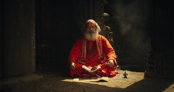 In an Ancient Temple, a Zoom in Portrait Features a Smiling Senior Hindu Monk Gazing at the Camera. Friendly Old Indian Man Poses, Seeking Guidance and Wisdom from His Religious Sacred Book