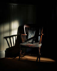 An empty chair in a dimly lit room the shadow cast by its occupant long gone but the unique indentations in the cushion still evident.